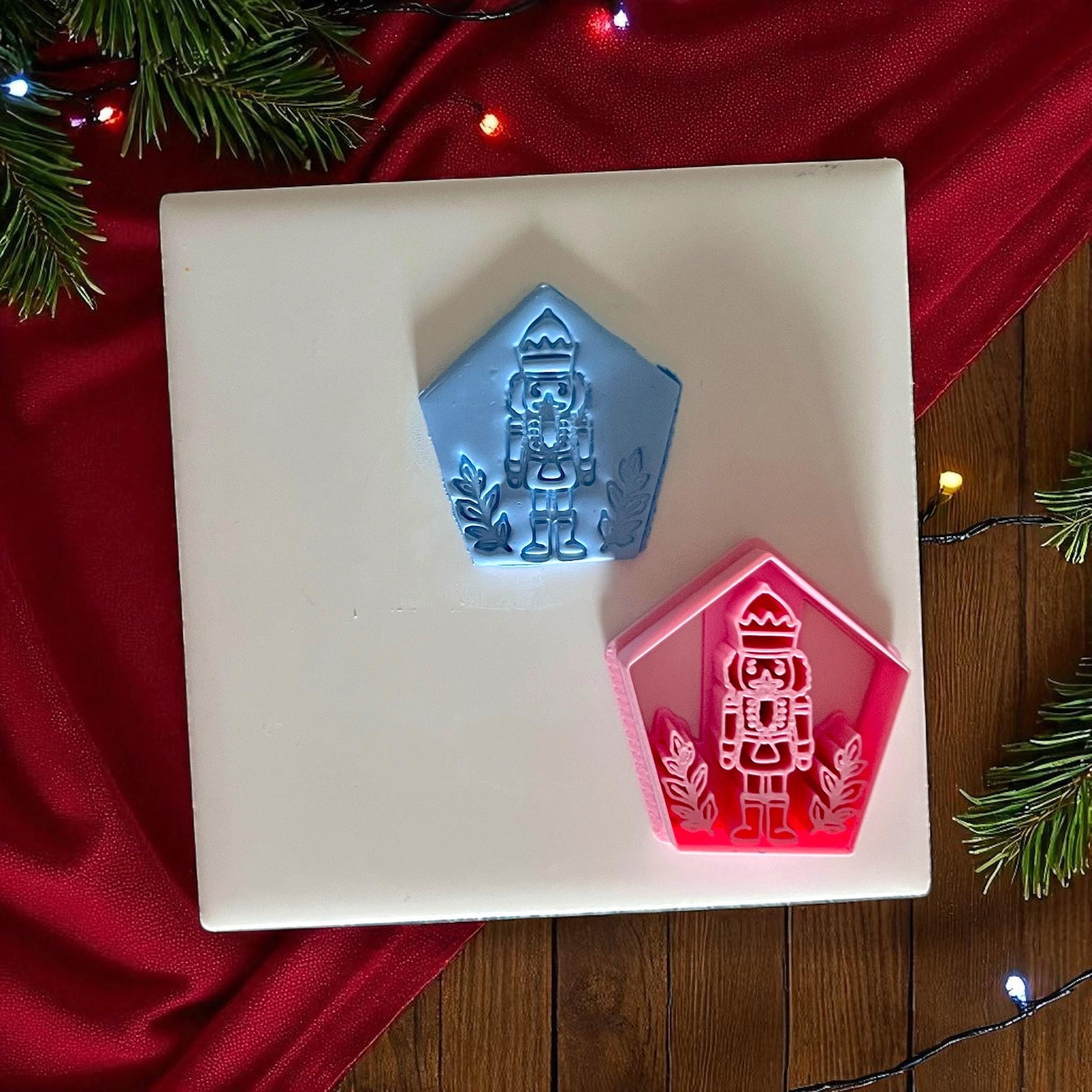 Blue nutcracker clay imprint and pink nutcracker cutter side by side on white tile with Christmas background.