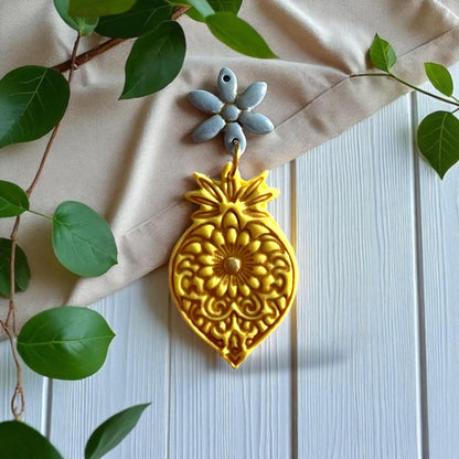 Large golden ornate mandala flower clay piece with blue floral connector on fabric and wood background.