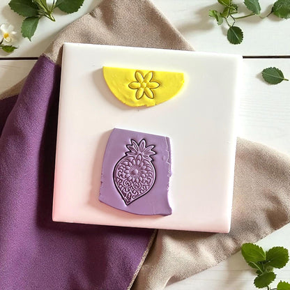 Yellow flower clay imprint and purple ornate mandala flower clay imprint on white tile with fabric.