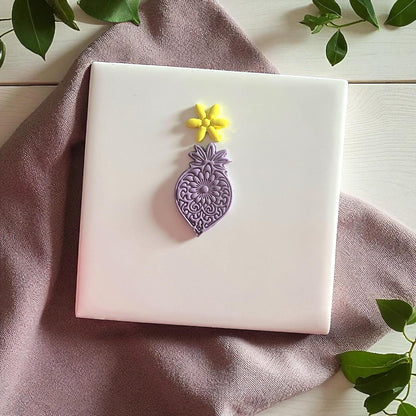Purple mandala flower clay imprint with yellow flower imprint on white tile and greenery.