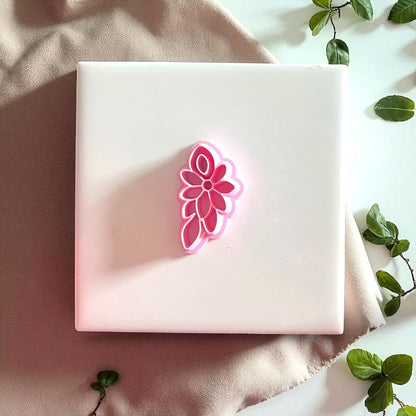Pink floral cluster cutter displayed on white tile with greenery and fabric.