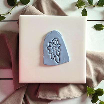 Blue clay imprint of floral cluster design on white tile with fabric and greenery.