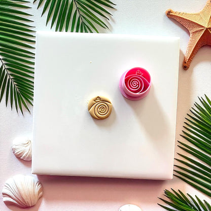 Pink paper boat cutter beside tan clay imprint with spiral wave design on white tile.