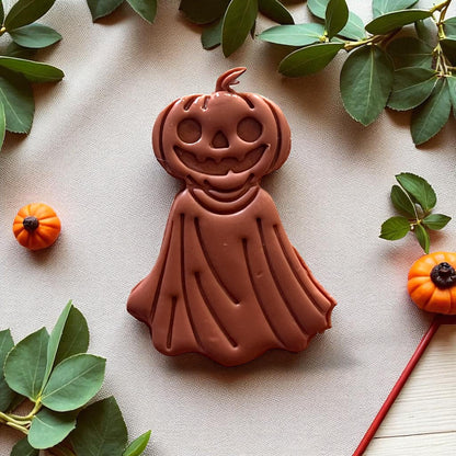 Large orange pumpkin ghost clay piece on fabric with pumpkins and greenery.