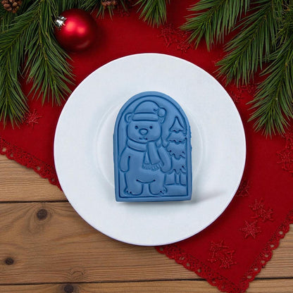Blue polar bear clay imprint and pink cutter side by side on white tile with Christmas greenery.