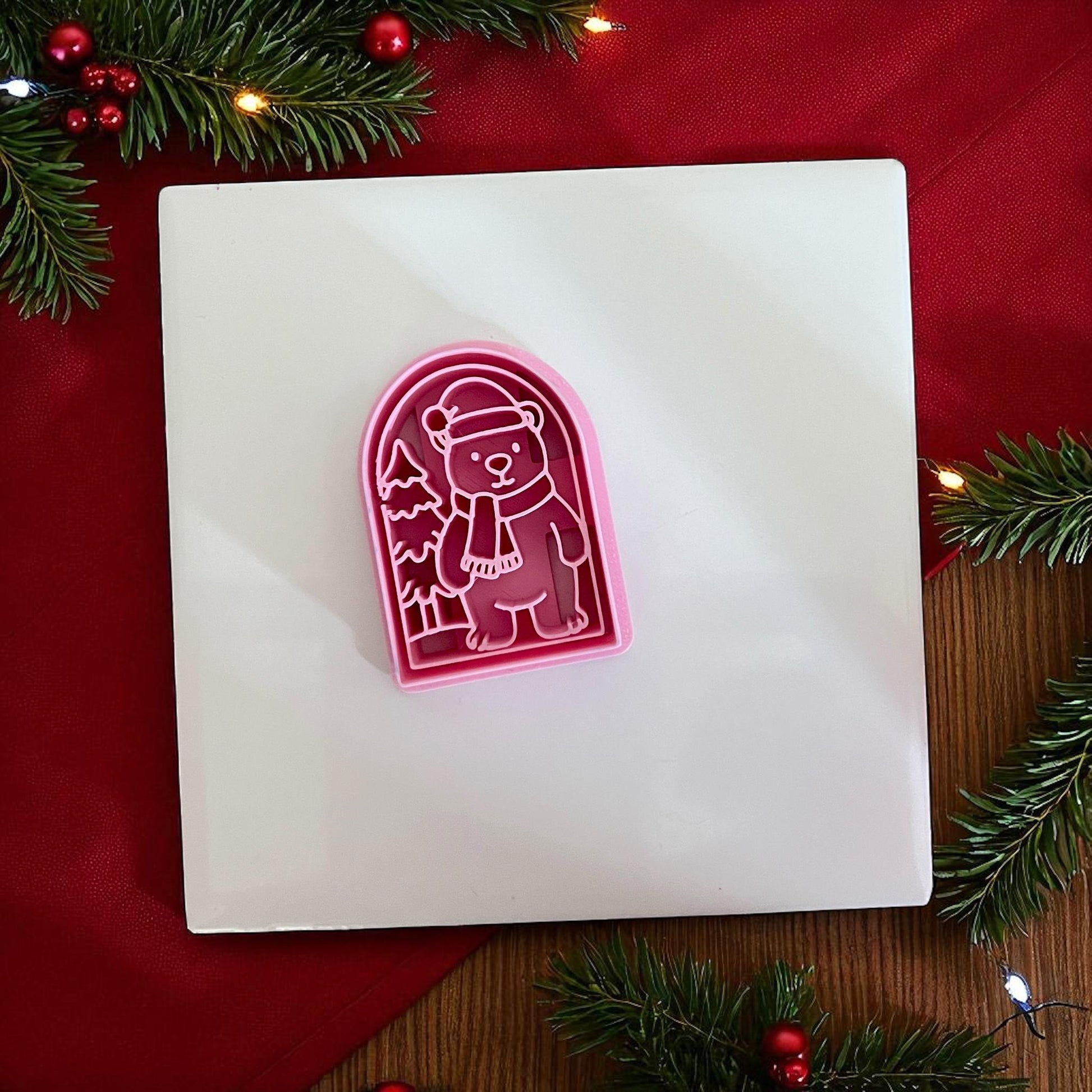 Pink Christmas polar bear clay cutter on white tile with red background and pine branches.
