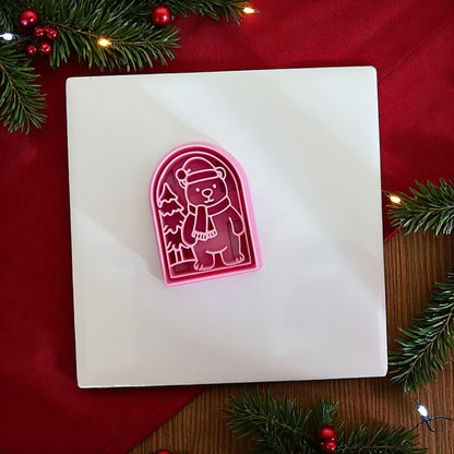 Pink Christmas polar bear clay cutter on white tile with red background and pine branches.