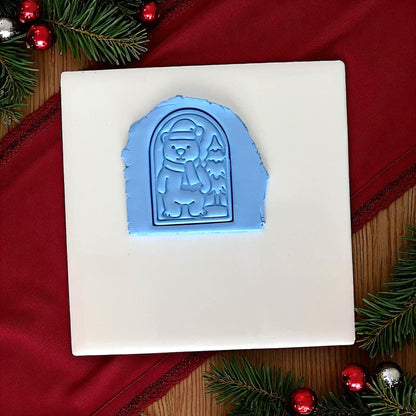 Blue polar bear clay imprint pressed into clay on white tile with red cloth and ornaments.