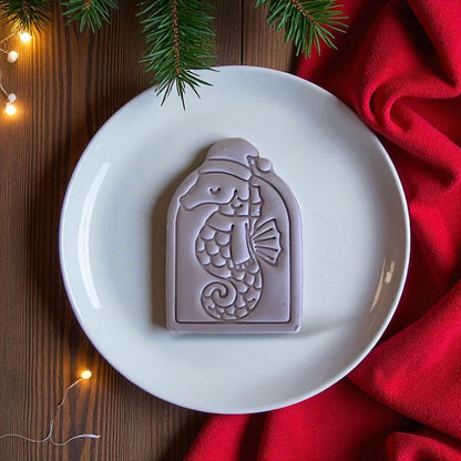 Purple seahorse clay imprint displayed on white plate with red fabric and pine greenery.