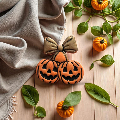 Pumpkin cherry bow clay imprint in orange and gold on wooden background with pumpkins and greenery.