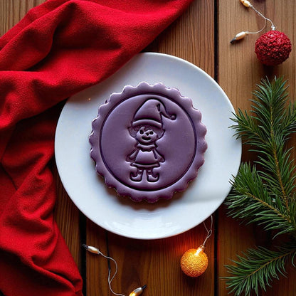 Purple elf clay imprint on clay slab with red fabric and holiday lights.