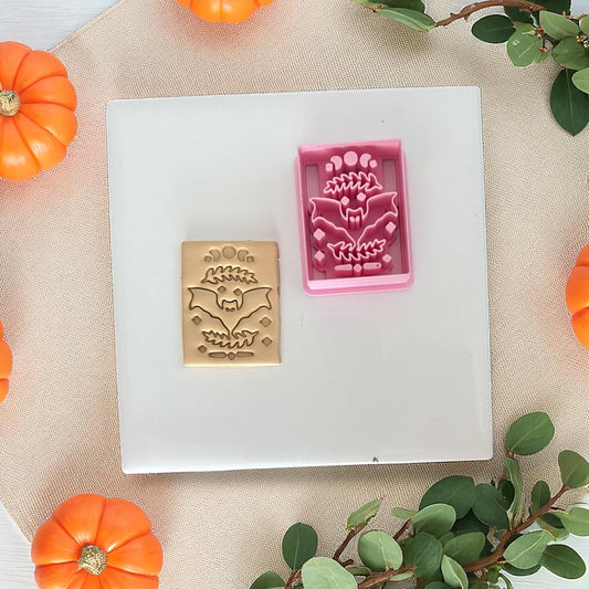 Pink bat rectangle clay cutter with beige clay imprint on white tile.