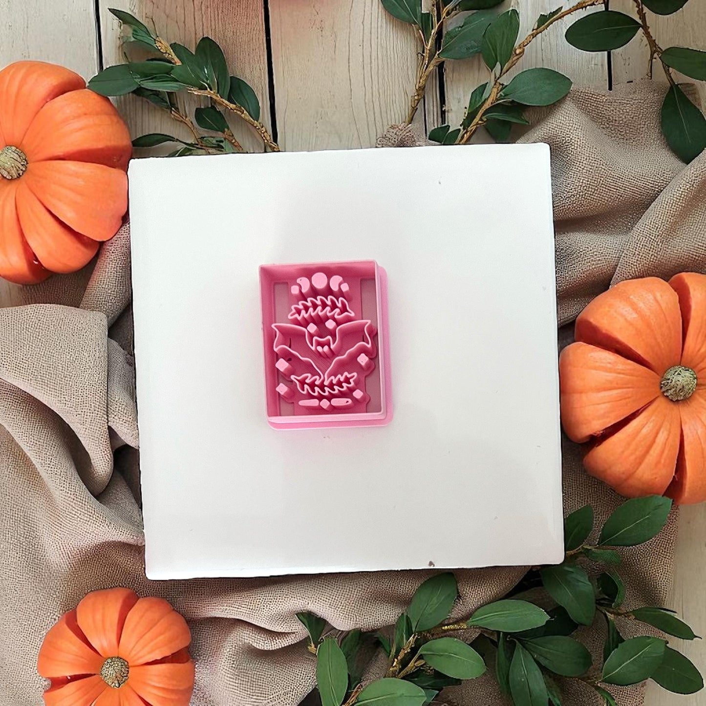 Pink rectangle bat cutter on white tile with pumpkins and greenery.