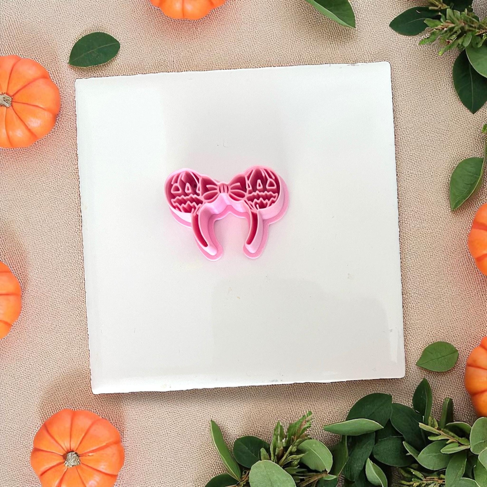 Pink pumpkin bow ears cutter on white tile with pumpkins around.