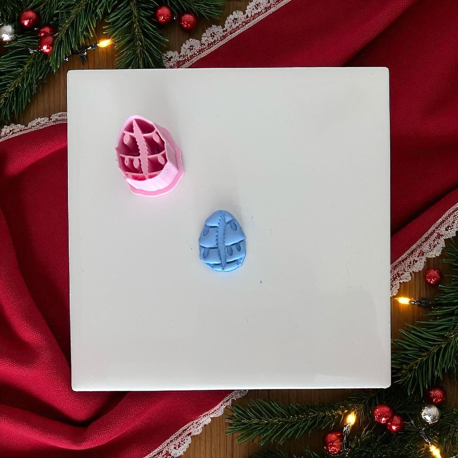 Small cowrie shell clay piece with Christmas lights on white tile with holiday greenery.