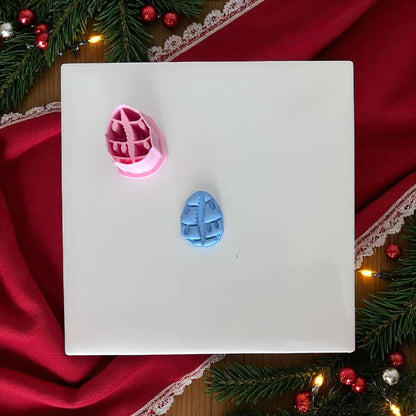 Small cowrie shell clay piece with Christmas lights on white tile with holiday greenery.