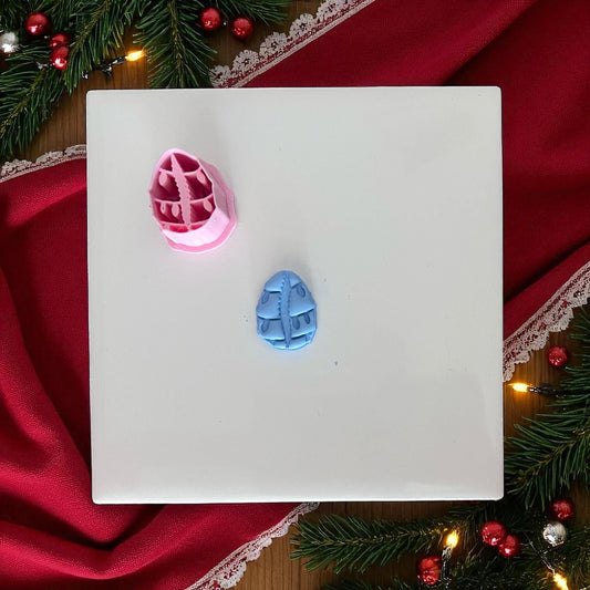 Small cowrie shell clay piece with Christmas lights on white tile with holiday greenery.