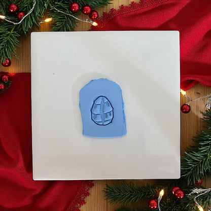 Cowrie shell clay design wrapped in red Christmas lights on wooden plate with red fabric.