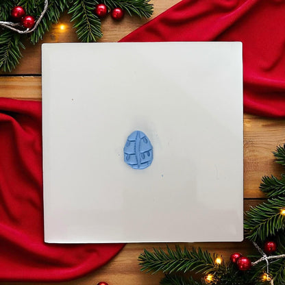 Cowrie shell clay ornament decorated with lights on wooden plate with pine branches and gift box.