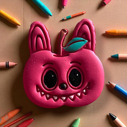 Large pink apple monster polymer clay piece surrounded by crayons