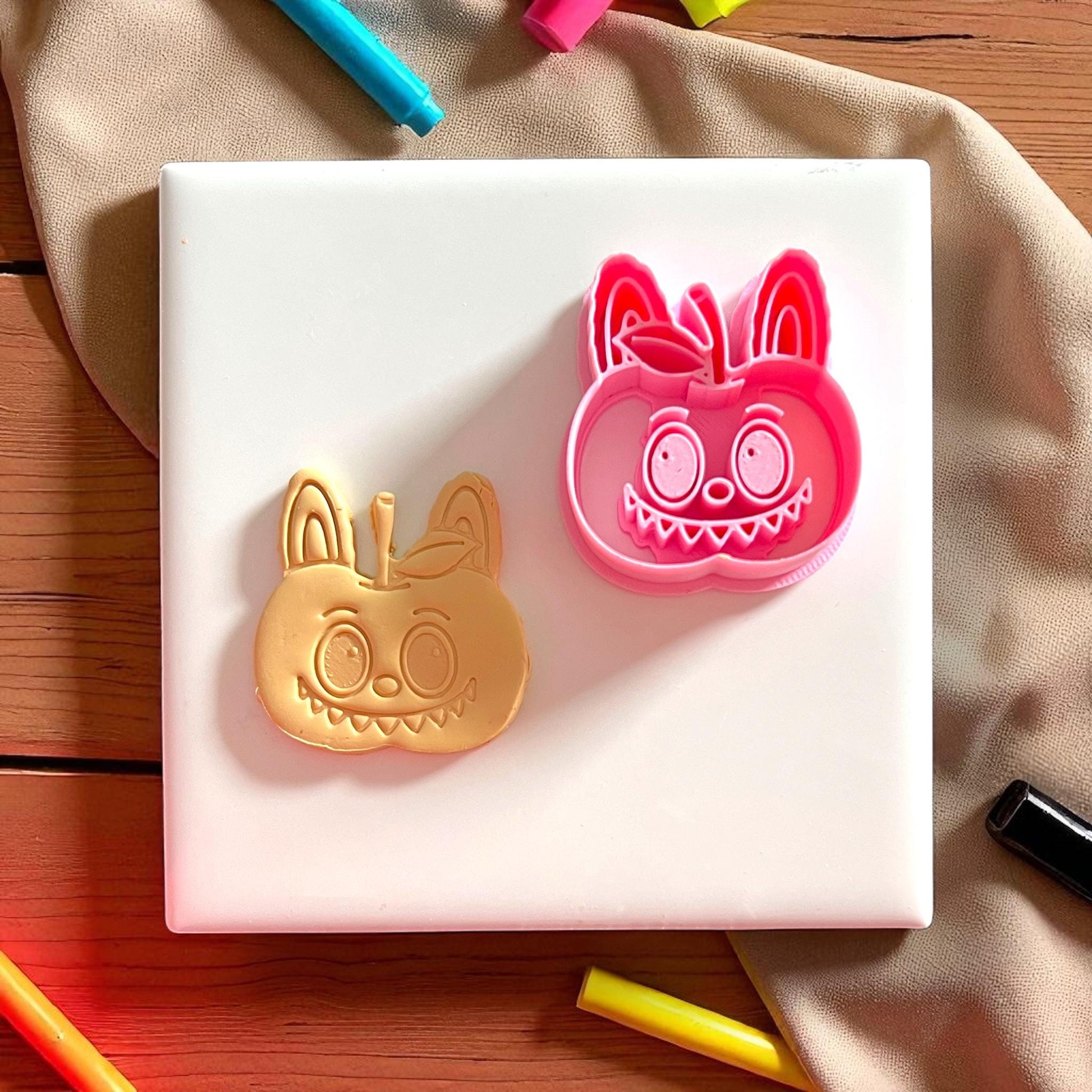 Pink polymer clay cutter with apple monster shape next to clay imprint