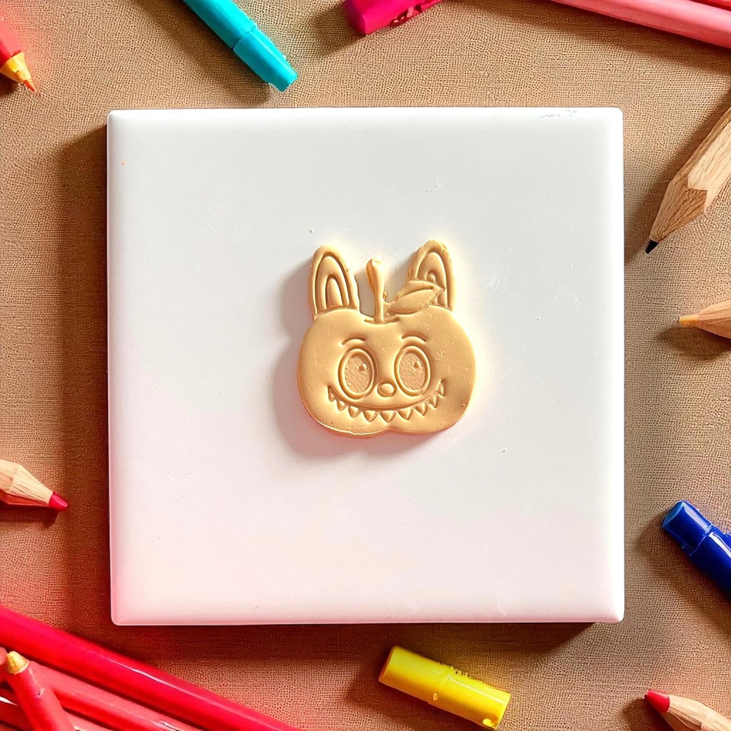 Small apple monster clay impression surrounded by colored pencils