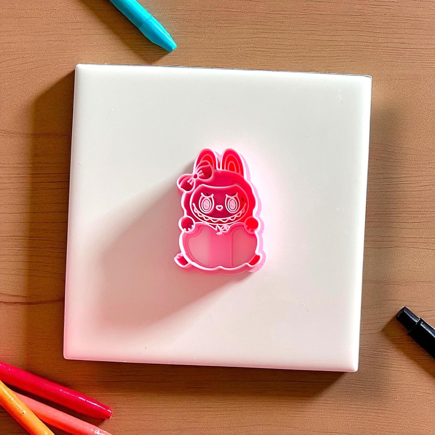 Pink apple holding monster cutter on white tile with colored pencils