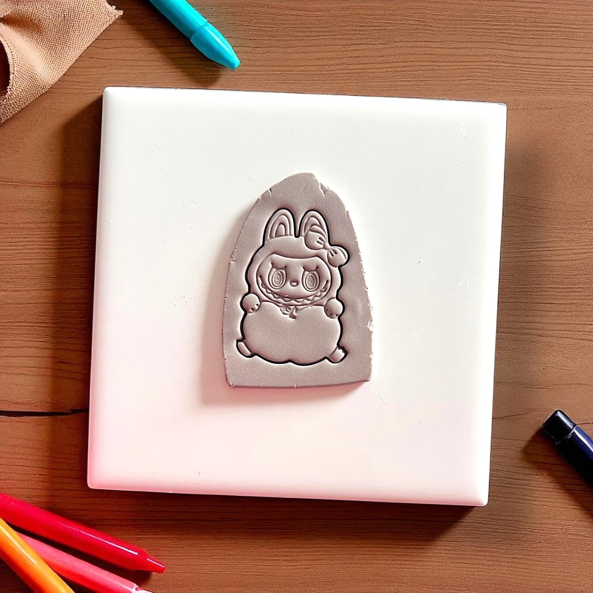 Apple holding monster clay imprint on white tile with colored pencils