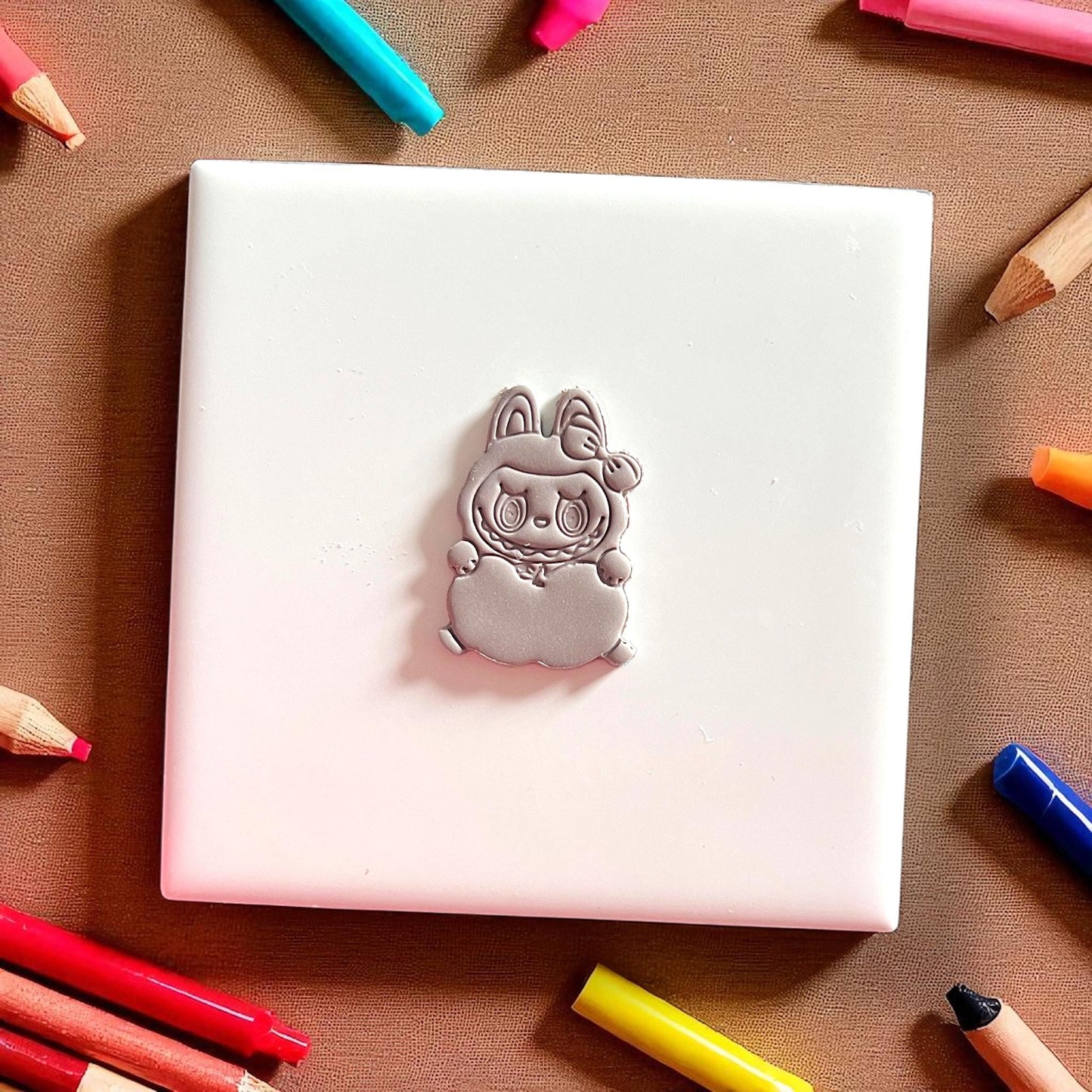 Apple holding monster clay shape on white tile with pencils around