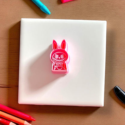 Pink polymer clay cutter in monster boy shape placed on white tile