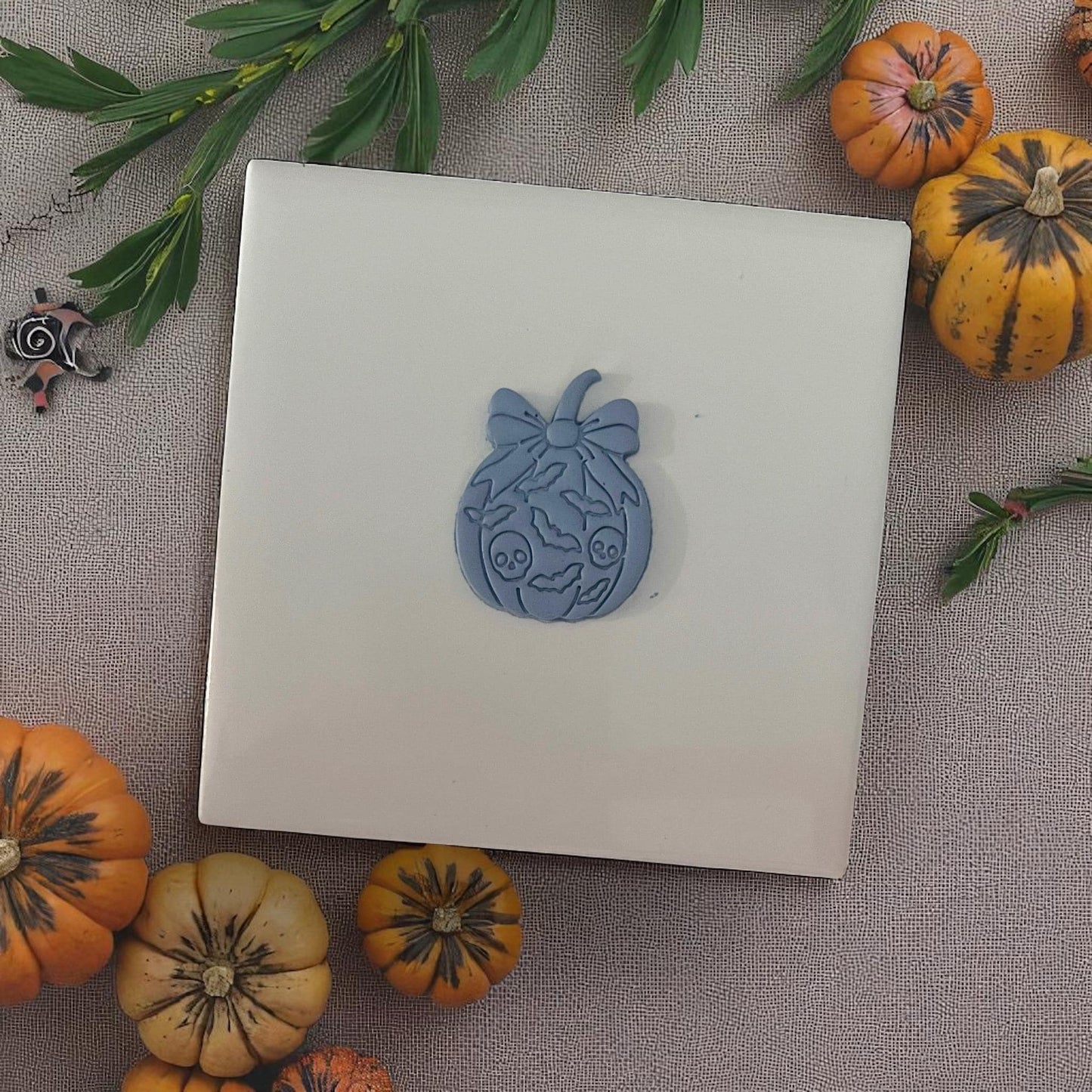 Halloween pumpkin bow cutter design on white tile surrounded by mini pumpkins