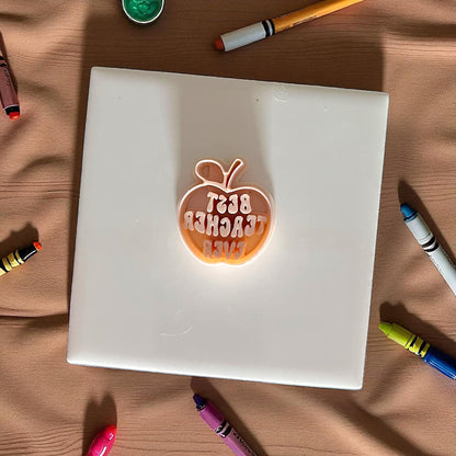 best teacher ever apple shaped polymer clay cutter on white tile surrounded by crayons