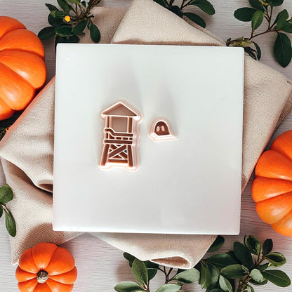 Ghost lifeguard tower clay piece next to matching cutters on a white tile with pumpkins.