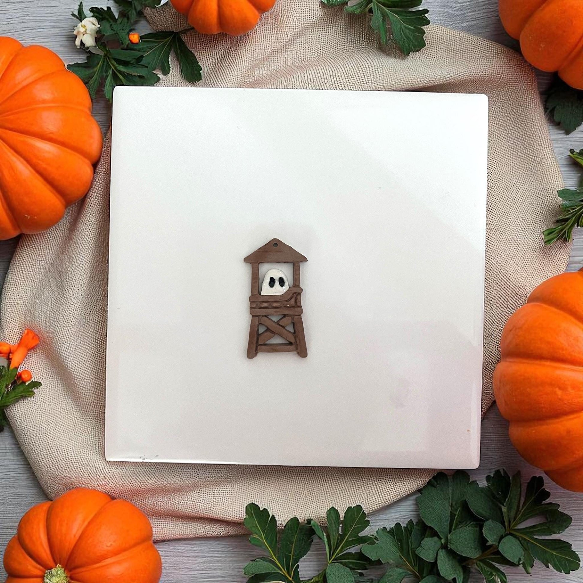 Empty ghost lifeguard tower cutters on a white tile surrounded by pumpkins.