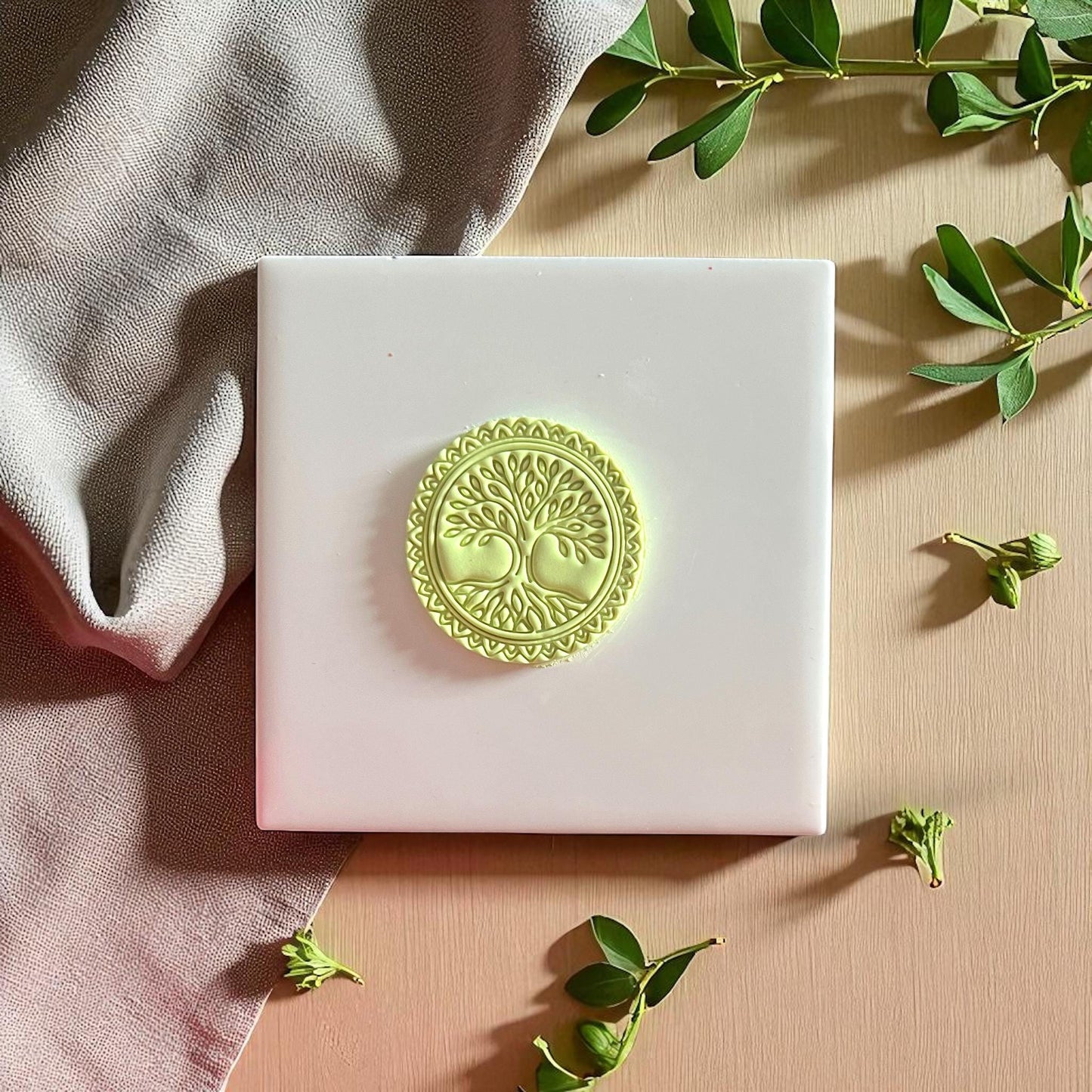 Round Tree of Life clay piece on white tile with fabric and leaves