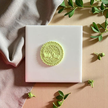 Round Tree of Life clay piece on white tile with fabric and leaves