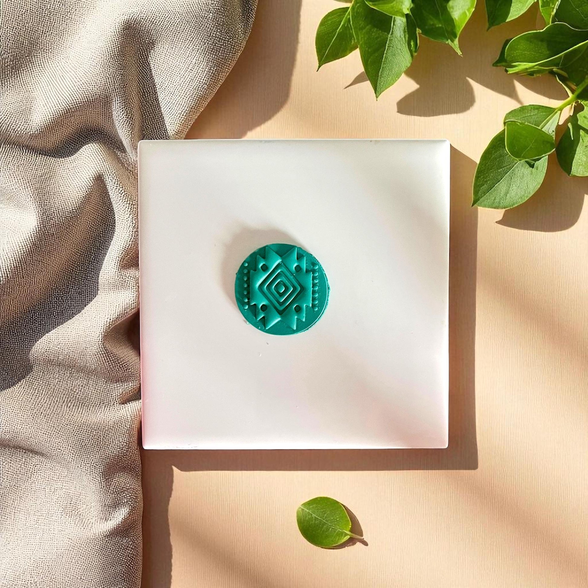 Teal clay imprint of round tribal diamond cutter pressed into clay, displayed on white tile and wooden board.