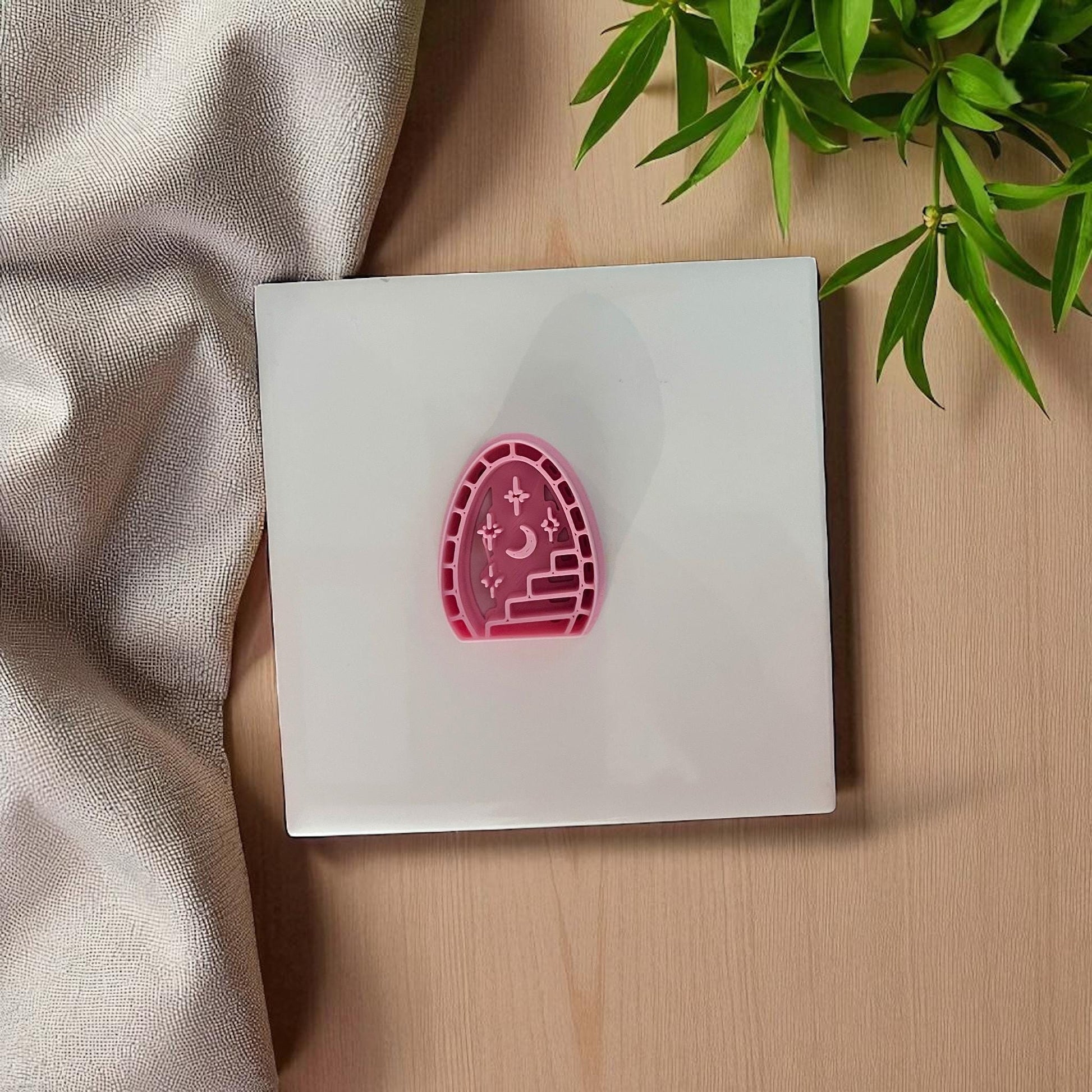 Pink arched cutter with stairway, moon, and stars on white tile with plant leaves in background.