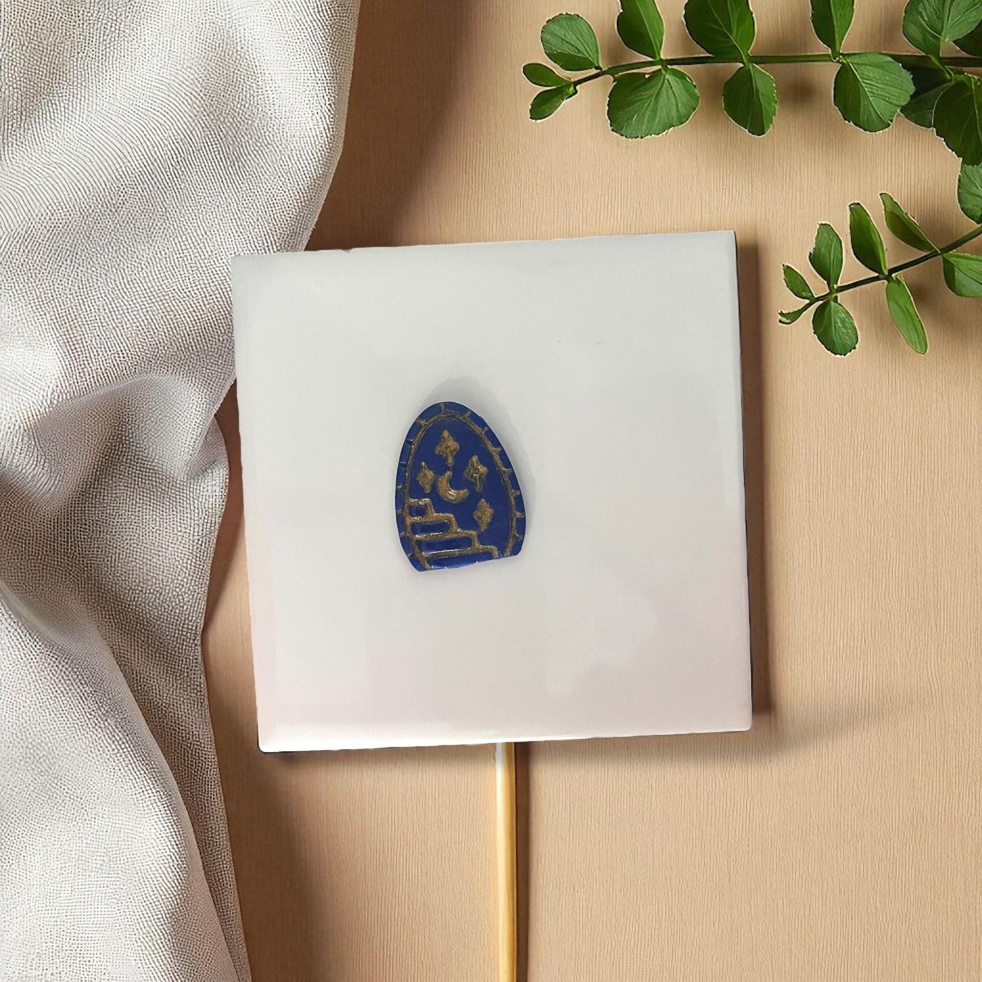 Blue clay imprint shaped like arched doorway with staircase, moon, and stars on white tile.