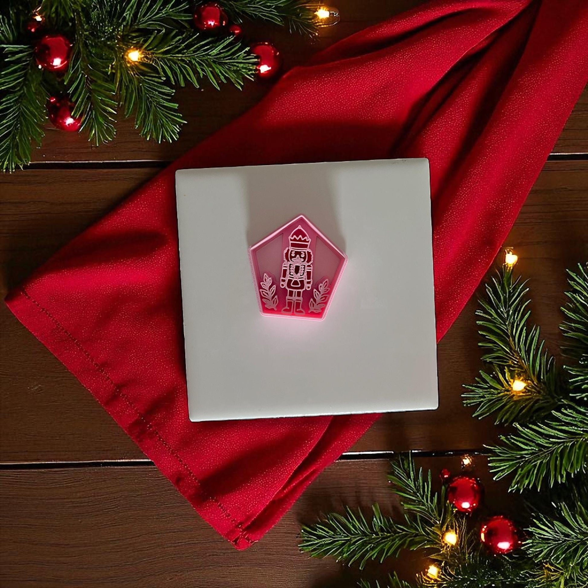 Pink nutcracker clay cutter on white tile with red cloth and holiday greenery.