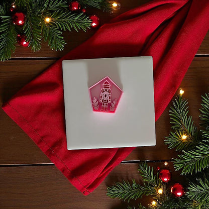 Pink nutcracker clay cutter on white tile with red cloth and holiday greenery.