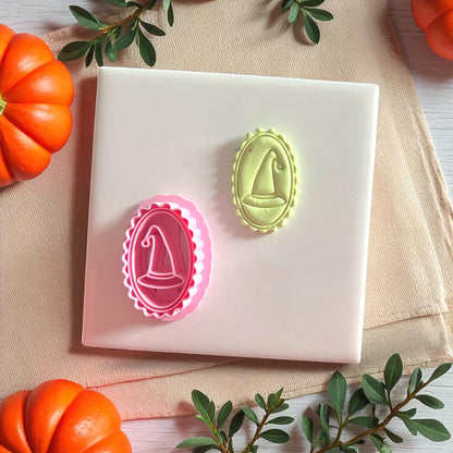 Pink cameo witch hat cutter and green clay imprint side by side on white tile with pumpkins.