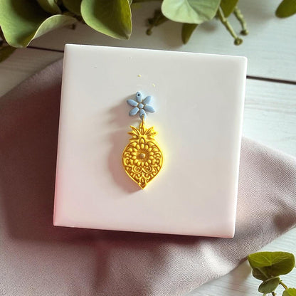 Golden mandala flower clay imprint with blue flower clay piece on white tile and fabric.