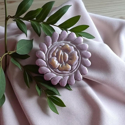 Large purple round flower clay piece with gold painted accents on fabric and greenery.