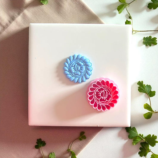 Pink flower cutter and blue clay imprint side by side on white tile with greenery.