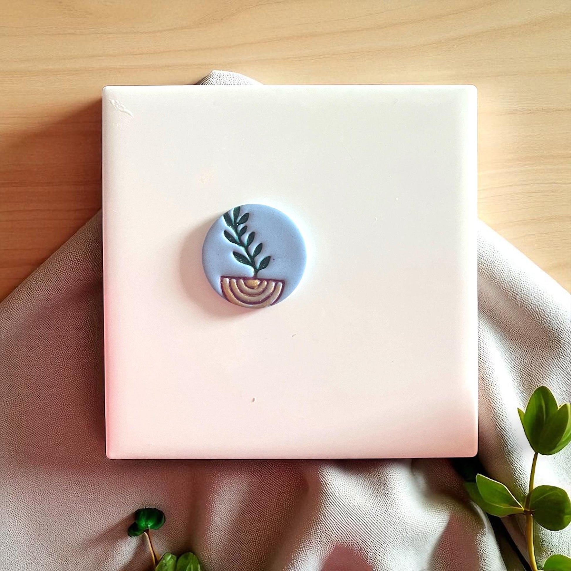 Blue clay imprint with painted plant and arch design on white tile and fabric.