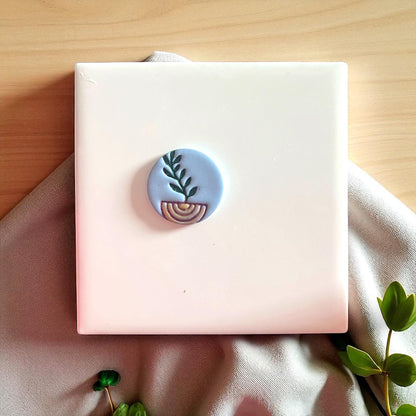 Blue clay imprint with painted plant and arch design on white tile and fabric.