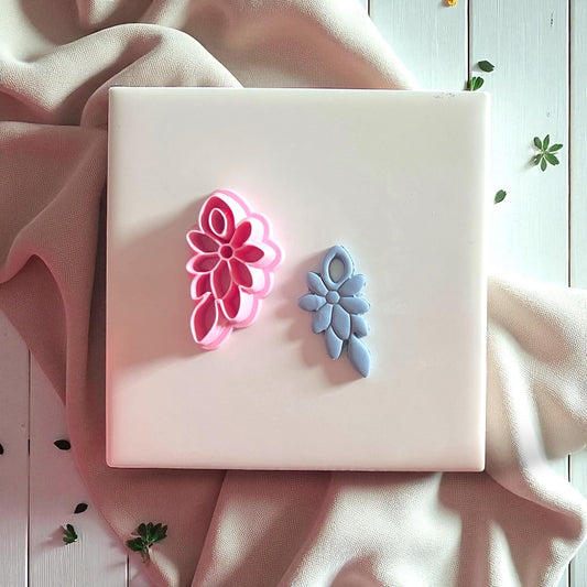Pink floral cluster cutter beside blue clay imprint on white tile with fabric background.