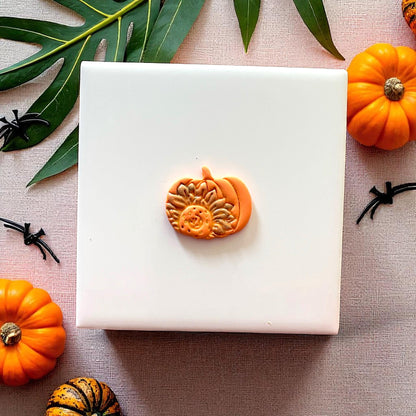 Small clay sunflower pumpkin design on white tile with leaves and pumpkins