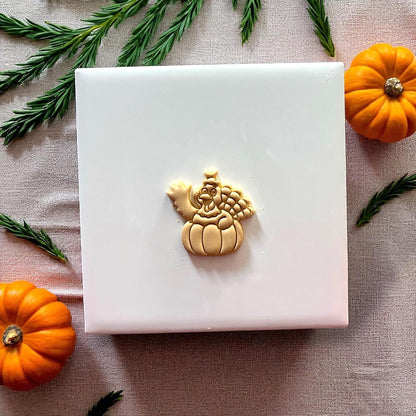 Small turkey pumpkin clay design on white tile with greenery